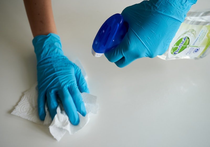 Gloved hands wiping a surface with cleaning spray