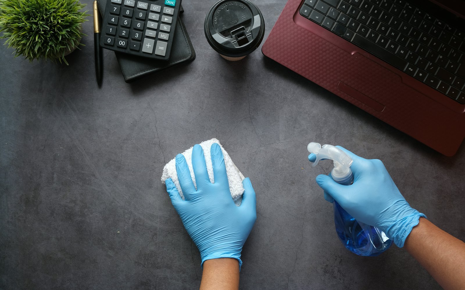 Cleaner in gloves wiping down an office desk and keyboard